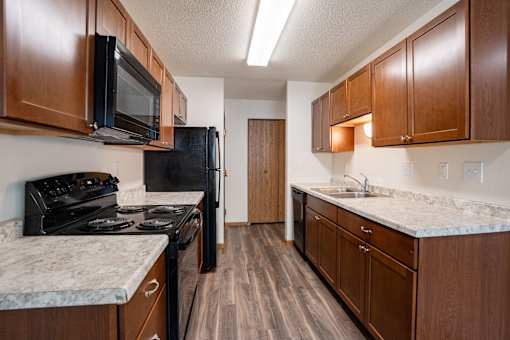A kitchen with dark wood cabinets and a black stove top oven. Grand Forks, ND Columbia West Apartments