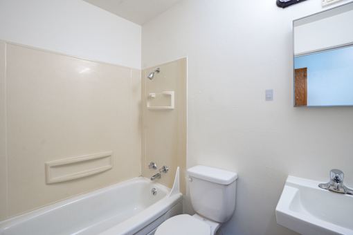 A white toilet sits next to a bathtub in a bathroom. Fargo, ND Morningside Apartments