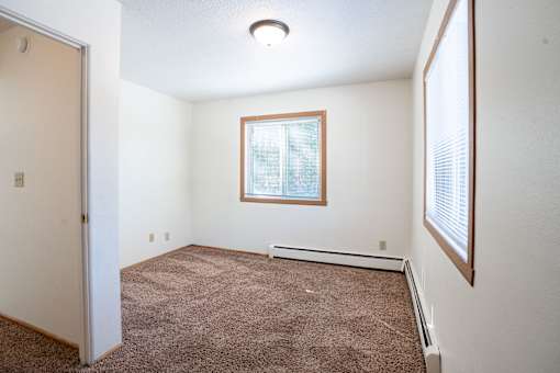 A room with a brown carpet and a window. Fargo, ND Morningside Apartments