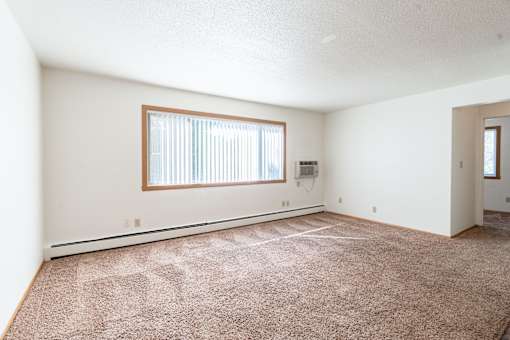 A room with a carpeted floor and a window with blinds. Fargo, ND Morningside Apartments