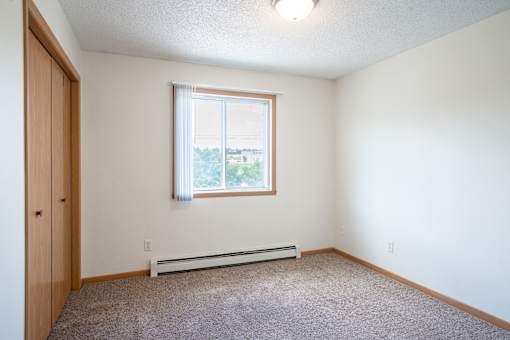 A room with a window and a carpeted floor. Bismarck, ND Sierra Ridge Apartments