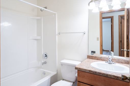 A white bathroom with a toilet, sink, and bathtub. Fargo, ND Long Island Apartments