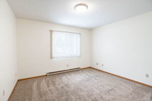 A room with a carpeted floor and a window with blinds. Fargo, ND Long Island Apartments