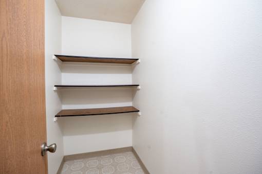 A white hallway with a brown door and three shelves. Fargo, ND Long Island Apartments