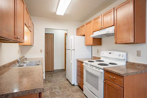 A kitchen with brown cabinets and white appliances. Fargo, ND Long Island Apartments