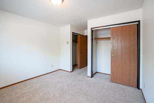 A room with a carpeted floor and a brown door. Fargo, ND West Oak Apartments