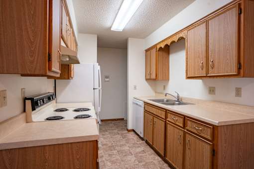 A kitchen with wooden cabinets and a white refrigerator. Fargo, ND West Oak Apartments
