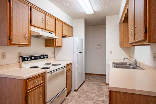 A kitchen with wooden cabinets and a white refrigerator. Fargo, ND West Oak Apartments