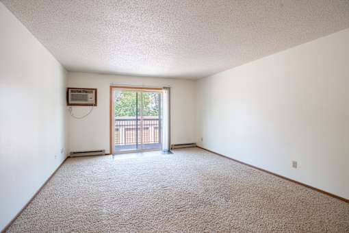 A room with a carpeted floor and a window with a view of a fence. Fargo, ND West Oak Apartments