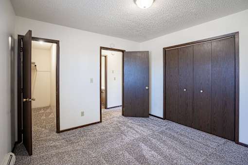 A room with a carpeted floor and three doors. West Fargo, ND Parkwest Gardens