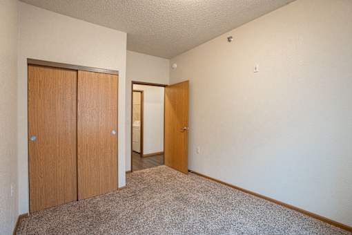 A room with a carpeted floor and two wooden doors. Fargo, ND North Sky II Apartments