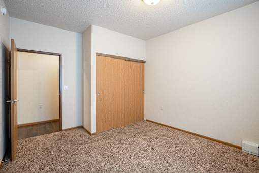 A room with a carpeted floor and two doors. Fargo, ND North Sky II Apartments