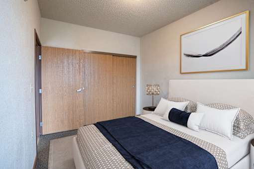 A bedroom with a bed, pillows, and a painting on the wall.