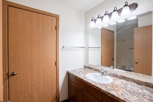 A bathroom with a sink, mirror, and wooden door. Fargo, ND Park Place Apartments