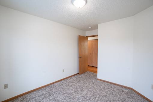 A room with a carpeted floor and a wooden door. Fargo, ND Park Place Apartments
