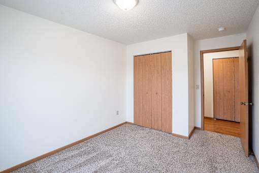 A room with a carpeted floor and two wooden doors. Fargo, ND Park Place Apartments