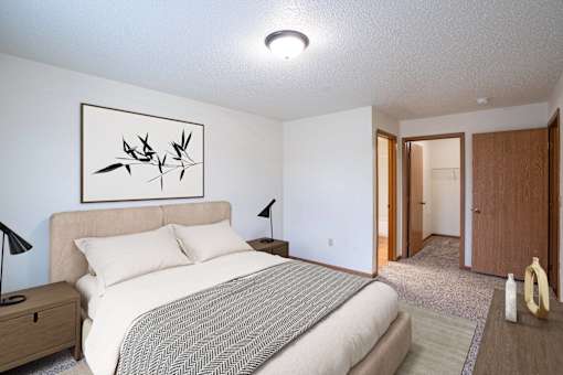 A bedroom with a bed, nightstand, lamp, and a framed picture on the wall. Fargo, ND Park Place Apartments