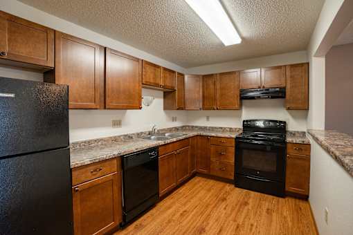 A kitchen with wooden cabinets and black appliances. Fargo, ND Park Place Apartments