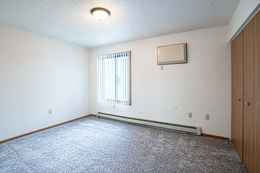 A room with a carpeted floor and a window with blinds. Fargo, ND Hazelwood Townhomes