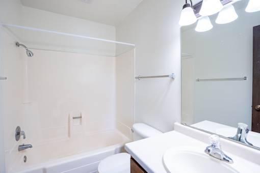 A white bathroom with a tub, sink, and mirror. Fargo, ND Summerfield Apartments