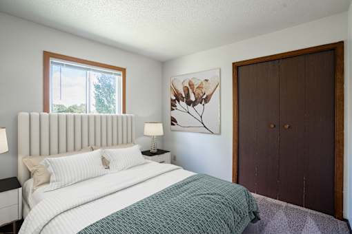A bedroom with a large bed and a painting on the wall. Fargo, ND Summerfield Apartments
