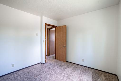 A room with a carpeted floor and a wooden door. Fargo, ND Summerfield Apartments