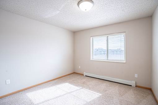 A room with a window and a carpet on the floor. Fargo, ND East Bridge Apartments