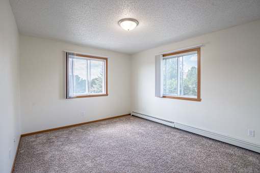 A room with two windows and carpeted floor. Bismarck, ND Sierra Ridge Apartments