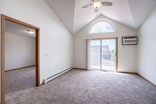 A room with a ceiling fan and a window with a view of a fence and a house. Bismarck, ND Sierra Ridge Apartments