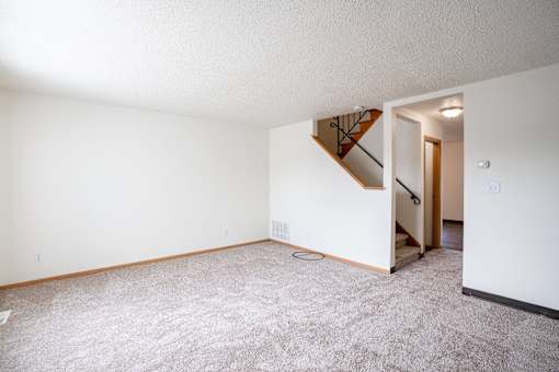 A living room with a carpeted floor and a staircase leading to another room. West Fargo, ND Sheyenne Terrace Townhomes
