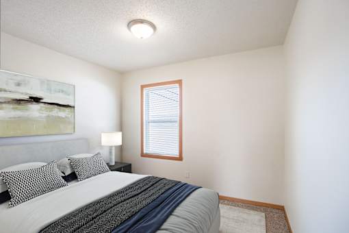 A bedroom with a bed, pillows, a lamp, and a painting on the wall. West Fargo, ND Sheyenne Terrace Townhomes
