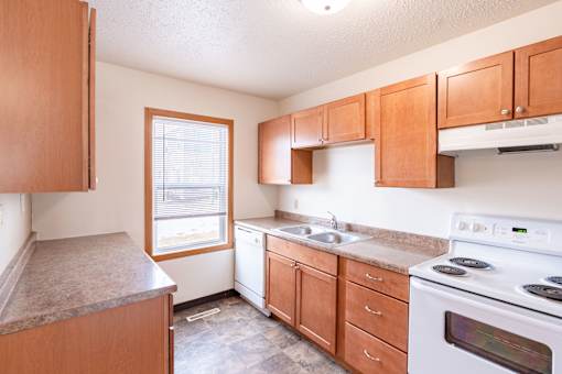 A kitchen with wooden cabinets and a white stove top oven. West Fargo, ND Sheyenne Terrace Townhomes