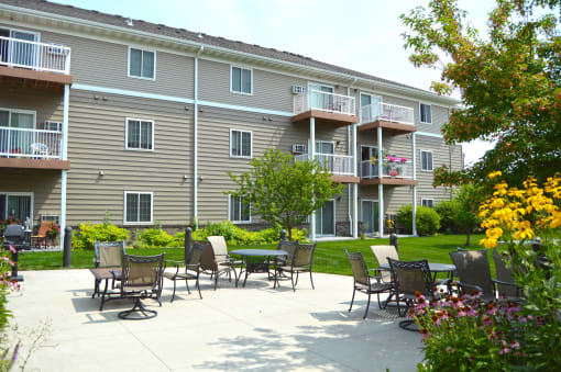 The exterior of a three level apartment building with a grass and patio area out front. Fargo, ND Crossroads Apartments