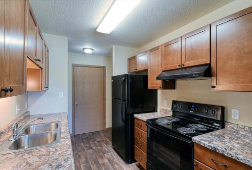 Grand Forks, ND Madison Apartments. A kitchen with black appliances and a closet.