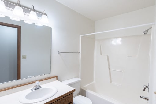 a bathroom with a shower sink and mirror and a toilet. Fargo, ND Rosegate Apartments