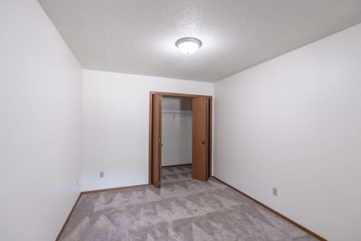 a room with a carpeted floor and a door to a closet. Fargo, ND Rosegate Apartments