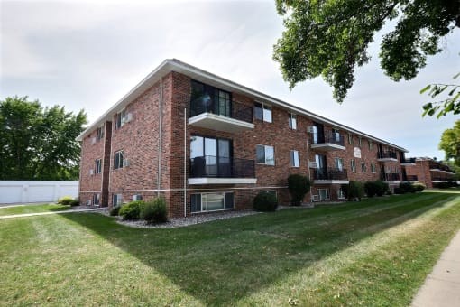 a red brick apartment building with a green lawn and a sidewalk. Fargo, ND Betty Ann Apartments