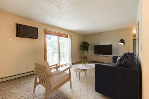 Bismarck, ND Brandon Apartments. A living room with a couch and a chair. A large sliding glass door allows natural light to fill the room.