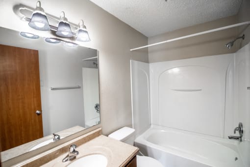 A bathroom with a sink and a tub and a mirror. Bismarck, ND Eastbrook Apartments.