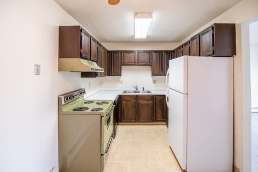 A kitchen with white appliances and brown cabinets and a refrigerator. Bismarck, ND Eastbrook Apartments .