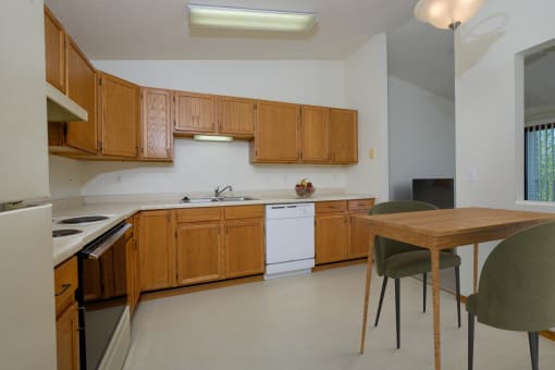 a kitchen with white appliances and wooden cabinets with a small dining table. Fargo, ND Bridgeport Apartments