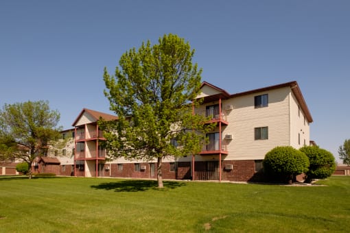 the outside of a three level apartment building with two trees out front. Fargo, ND Bridgeport Apartments