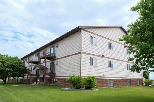 the exterior of a building with a green lawn and trees. Fargo, ND Carlton Place Apartments