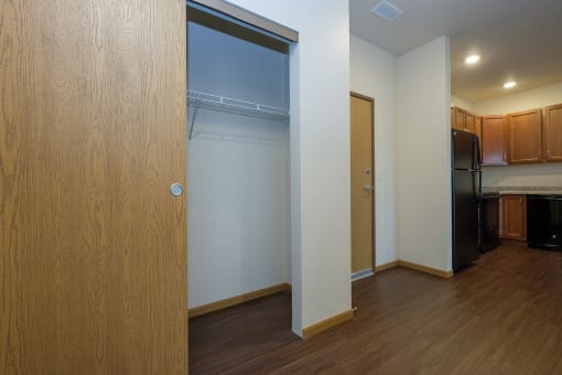 a door opens into a kitchen with a black refrigerator and a wood floor. Fargo, ND North Sky Apartments