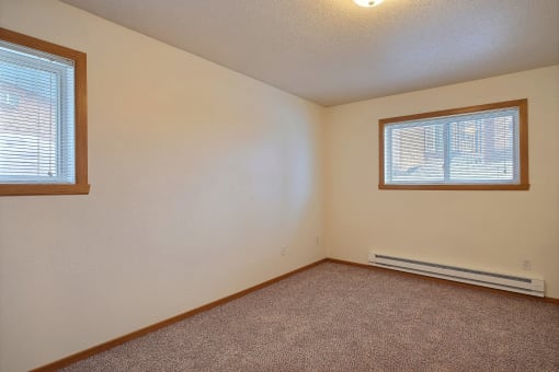 a bedroom with two windows and carpeted floors. Fargo, ND Dakota Manor Apartments