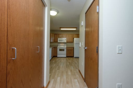 a hallway with closet doors and the kitchen in the background. Fargo, ND Crossroads Apartments