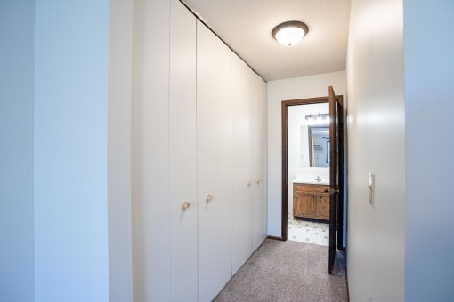 a hallway with white cabinets and a bathroom with a mirror.  Eagan, MN Glen Pond Apartments
