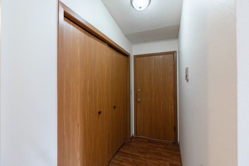an empty hallway with a wooden door and a closet. Fargo, ND Rosegate Apartments