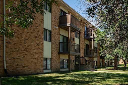 A brick building with balconies and trees in front. Bismarck, ND Garden Grove Apartments