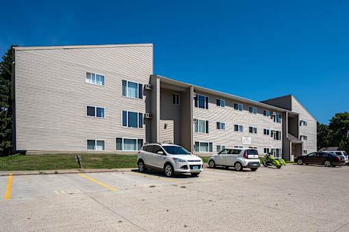 A grey building with a parking lot in front of it. Bismarck, ND Bradbury Apartments